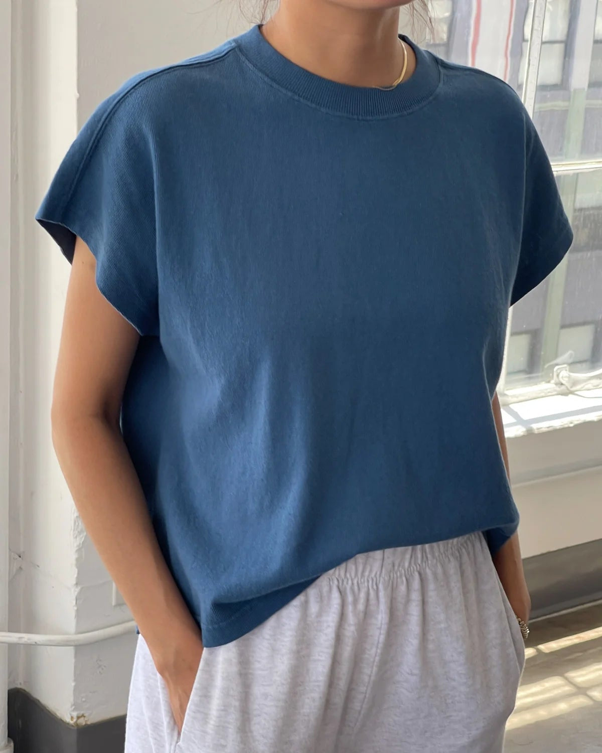 Person wearing a blue top and gray pants standing indoors.
