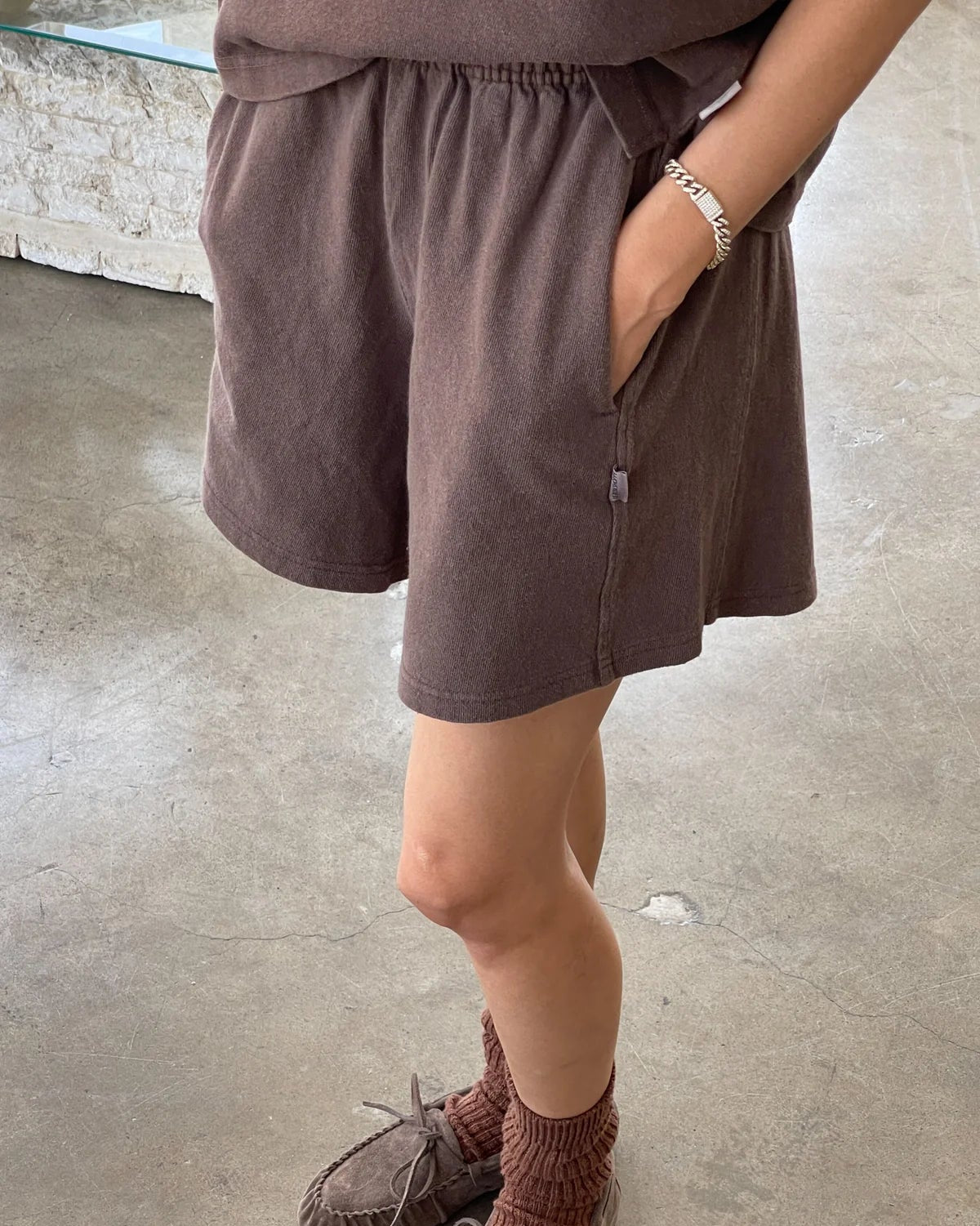 Person wearing brown shorts and slippers on a concrete floor.