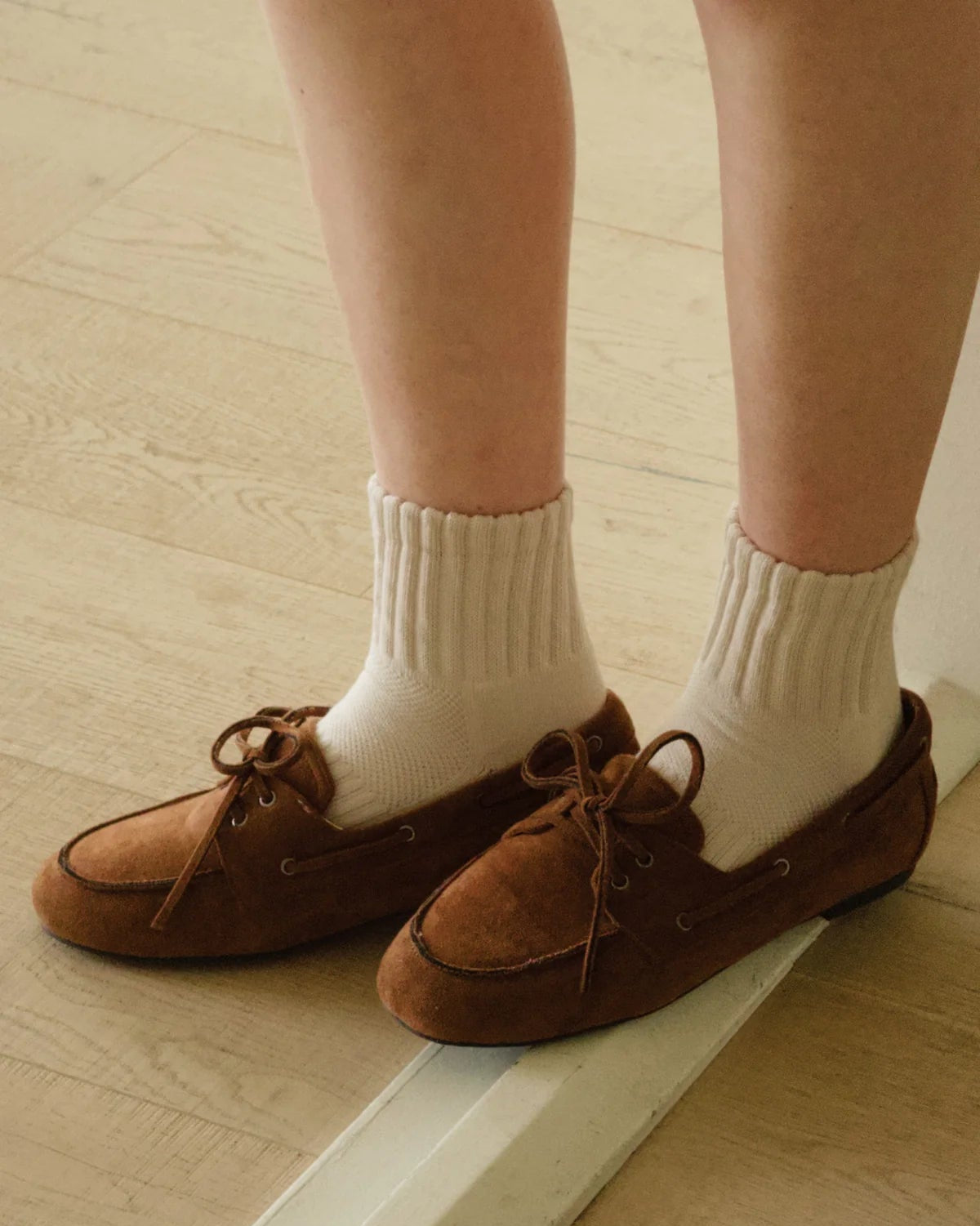Brown loafers worn with white socks on a wooden floor